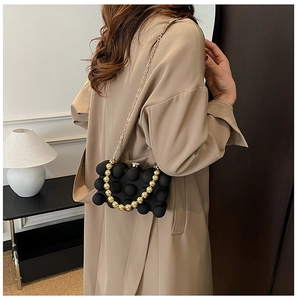 Detailed shot of black spherical textured clutch with gold bead handle and chain strap