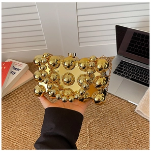 Detail of a gold metallic evening clutch bag featuring 3D spheres and a chain strap