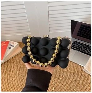 Close-up of black 3D textured acrylic evening bag with gold bead handle and chain strap