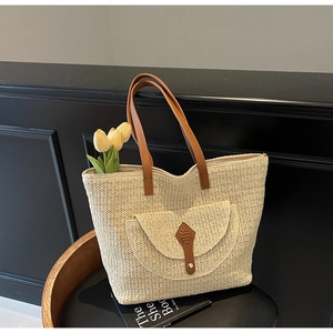 Gros plan détaillé du sac cabas en paille avec anses en cuir marron et poche avant décorée