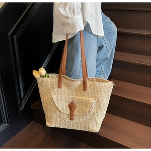 Détail d'un sac cabas en paille beige avec anses en cuir marron et poche frontale