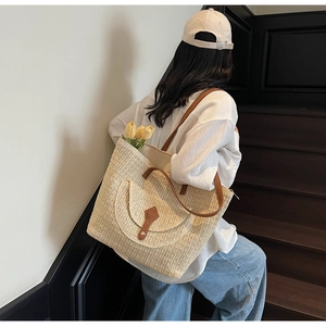 Détail du cabas en paille tissée avec bretelles en cuir marron et poche avant décorée