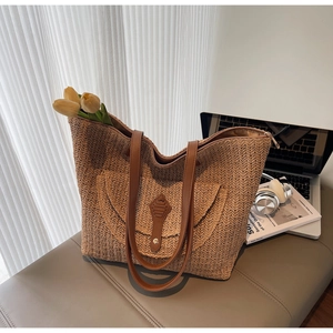 Détail d'un sac cabas en paille avec anses en cuir marron et poche avant décorative