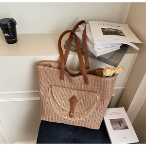 Détail d'un grand sac cabas en paille avec lanières en cuir brun et poche avant