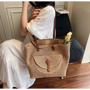 Détail d'un grand sac cabas en paille tressée avec poche avant en cuir et longues bandoulières