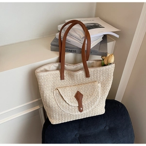Détail du sac cabas en paille avec accents en cuir marron et poche avant pour la plage