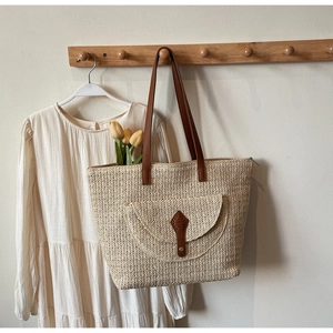 Détail d'un sac cabas tissé beige avec lanières en cuir marron suspendu sur une robe