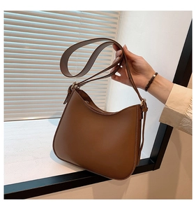 Detail of a brown crescent shoulder bag with smooth texture and golden hardware accents