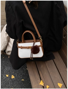 Détail d'un sac à main tissé blanc avec garniture en cuir brun et breloque en peluche