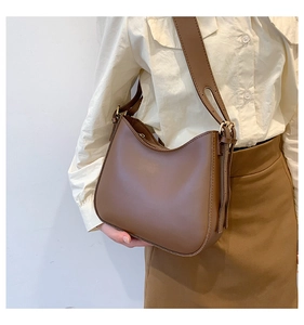 Brown leather half-moon crossbody bag with wide adjustable shoulder strap on model