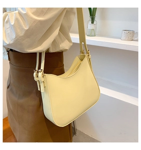 Detail of a creamy yellow crescent shoulder bag with metallic buckle and adjustable strap
