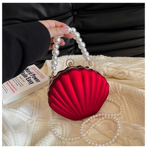Detail of red shell-shaped evening clutch with pearl handle and metallic clasp