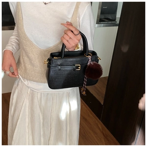 Detail of black woven shoulder bag featuring gold hardware and a brown faux fur pompom charm