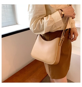 Minimalist beige saddle bag with adjustable strap worn by model in a bright indoor setting