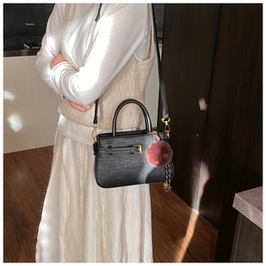 Detail of black woven shoulder bag with golden hardware and plush pompom charm accessory