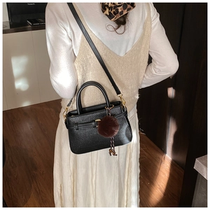 Detail of black woven shoulder bag featuring a brown faux fur ball charm on wood floor