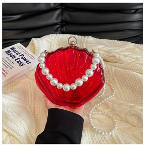 Detail of red shell-shaped evening bag with pearl handle and texture on clear acrylic