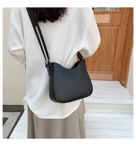 Minimalist black leather crossbody bag with adjustable gold buckle on a shoulder model