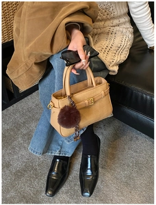 Close-up of beige crossbody bag with textured finish and brown faux fur pompom charm