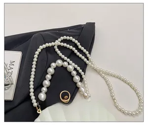 Detail of elegant pearl chain straps on white shell evening bag with golden metal hardware
