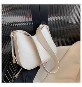 Detail of a minimalist beige crescent bag featuring wide shoulder strap and gold hardware