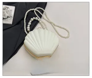 Detail view of cream shell evening bag with pearl handle and shoulder chain next to a phone