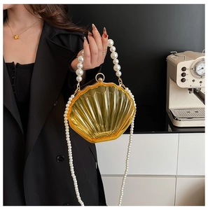 Detail of yellow shell-shaped acrylic handbag with pearl handle and beaded chain