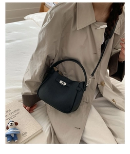 Gros plan d'un sac seau en cuir noir à grain de litchi porté avec un trench-coat beige