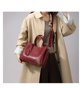 Close-up of red crocodile pattern tote bag with golden base studs on beige trench coat
