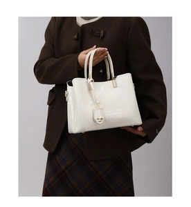 Detail of white crocodile-embossed tote bag with golden hardware and twin handles