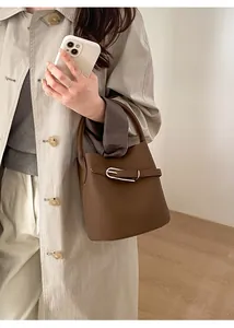 Sac seau marron à motif litchi porté par un mannequin en trench-coat beige chic