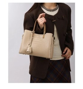 Detail of beige crocodile embossed handbag with gold hardware and petal charm on model