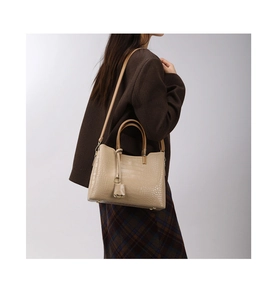 Side view of beige crocodile embossed handbag with handles and detachable strap on model