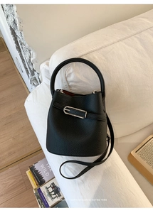 Vue détaillée du sac seau noir en cuir grainé avec boucle argentée sur un canapé blanc