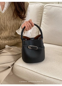 Gros plan du sac seau en cuir noir avec boucle en métal argenté dans un décor de vie