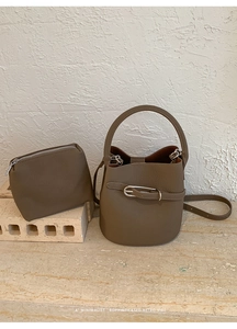 Détail du sac seau à texture litchi et de sa pochette assortie sur marbre blanc