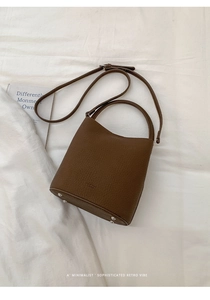 Gros plan du sac seau en cuir marron grainé avec pieds en métal sur tissu blanc