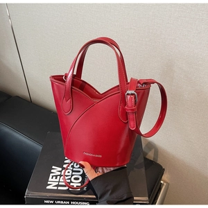 Detail of red leather bucket bag with silver hardware and adjustable strap on a book