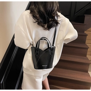 Detail of black bucket bag with Fashion & Bags text and V-shaped opening on a model