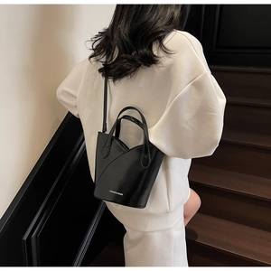 Detail of black leather bucket bag with petal edge and white fashion logo on stairs