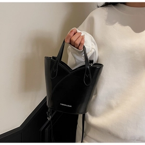 Detail of black glossy patent leather bucket bag with wavy rim and adjustable shoulder strap