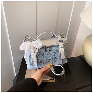 Detalle de bolso caja de mezclilla azul con pedrería, lazo de encaje y dije de perla