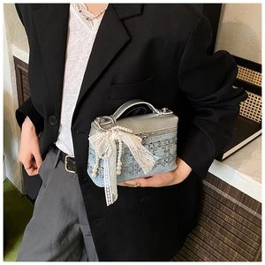 Detalle de bolso vaquero con tapa metálica plateada y colgante de lazo con perlas