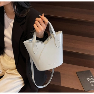 Detail of light grey bucket bag with wavy rim shown on a stylish model on stairs