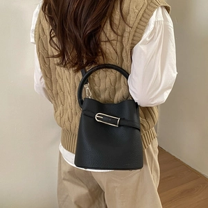 Sac seau noir chic avec texture grainée et boucle argentée porté par un mannequin