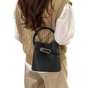 Sac seau chic en cuir litchi noir avec boucle argentée porté en bandoulière par un mannequin