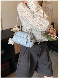 Close-up of light blue quilted crossbody bag with gold chain and sheep charm