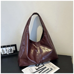 Detail einer burgunderfarbenen, glänzenden Hobo-Tasche aus plissiertem Lackleder