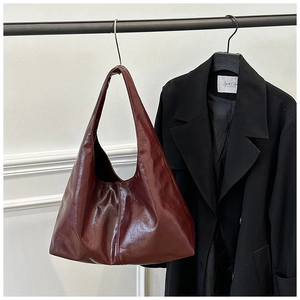 Detailaufnahme einer hochglänzenden weinroten Hobo-Tasche neben einem schwarzen Wollmantel
