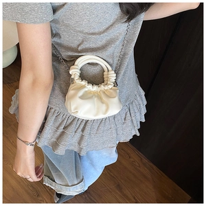 Close-up of a creamy white PU leather mini bag with soft pleats and silver chain strap